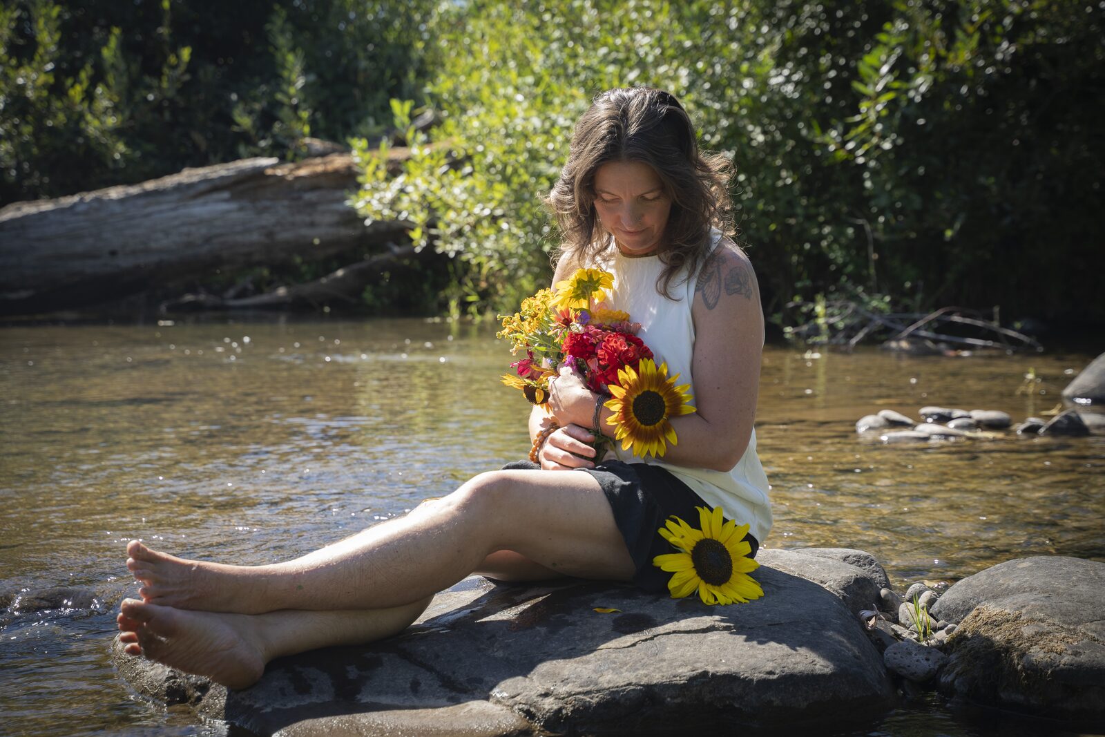 Bethany sitting by a river holding a bouquet of sunflowers