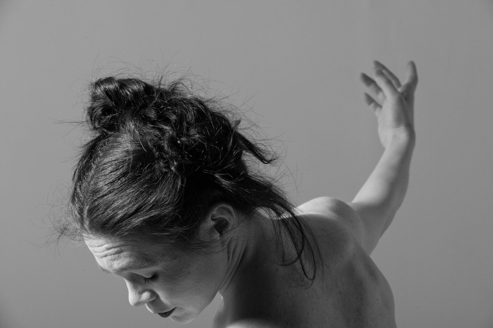 A woman in profile with head bowed and one arm lifted
